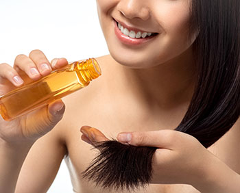 cropped shot of smiling woman pouring oil on split ends isolated on white